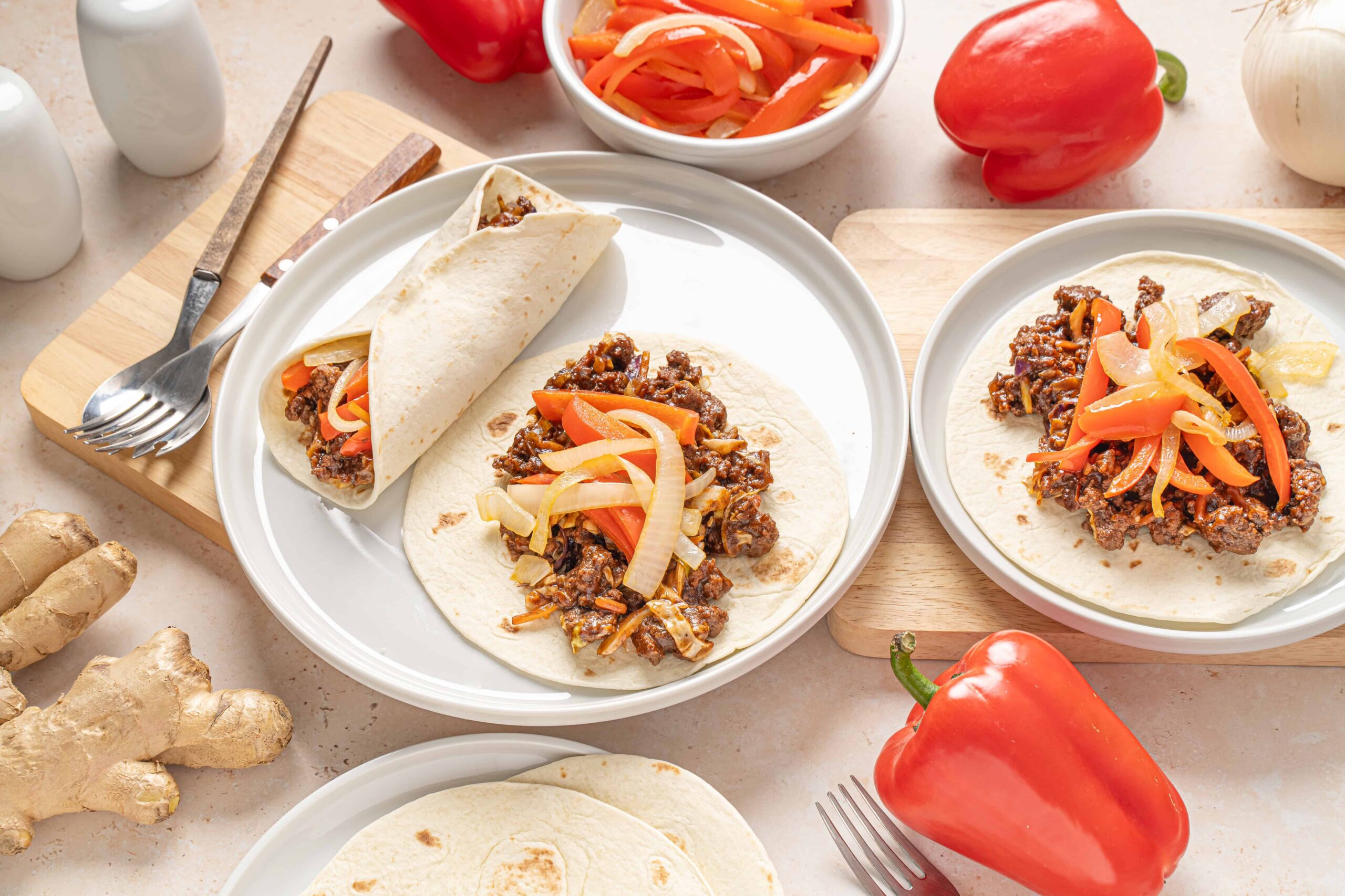 Savory beef taco filling with fresh vegetables on soft flour tortillas, ready to be rolled for delicious homemade tacos. Fresh peppers and ginger enhance the vibrant, flavorful presentation.