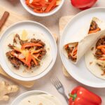 Sautéed beef and vegetable tacos with fresh peppers and garlic, served on white plates with wooden cutting boards, forks, and colorful ingredients for authentic Mexican cuisine.