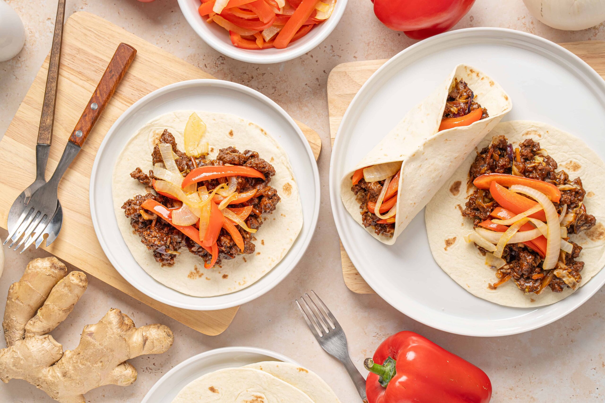 Sautéed beef and vegetable tacos with fresh peppers and garlic, served on white plates with wooden cutting boards, forks, and colorful ingredients for authentic Mexican cuisine.
