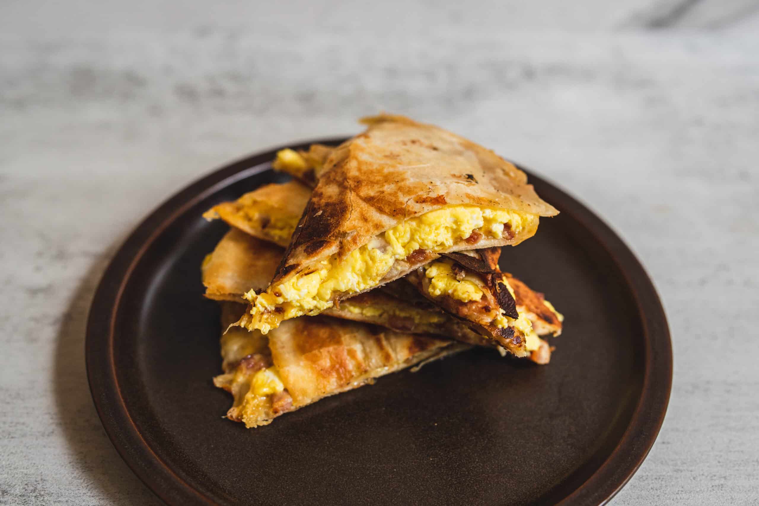 Fluffy breakfast quesadillas filled with scrambled eggs, melted cheese, and bacon served on a black plate. Perfect for a quick, delicious morning meal or brunch.