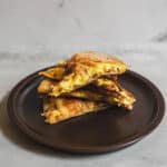 Crispy breakfast quesadilla with scrambled eggs, cheese, and bacon on a dark plate against a rustic gray background.