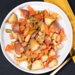 Roasted potato hash with carrots, celery, onions, and seasoned potatoes on a white plate, served with a gold fork on a yellow napkin.