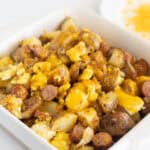 Creamy scrambled eggs with sausage and potatoes served in a white baking dish, garnished with melted cheese, perfect for breakfast or brunch.