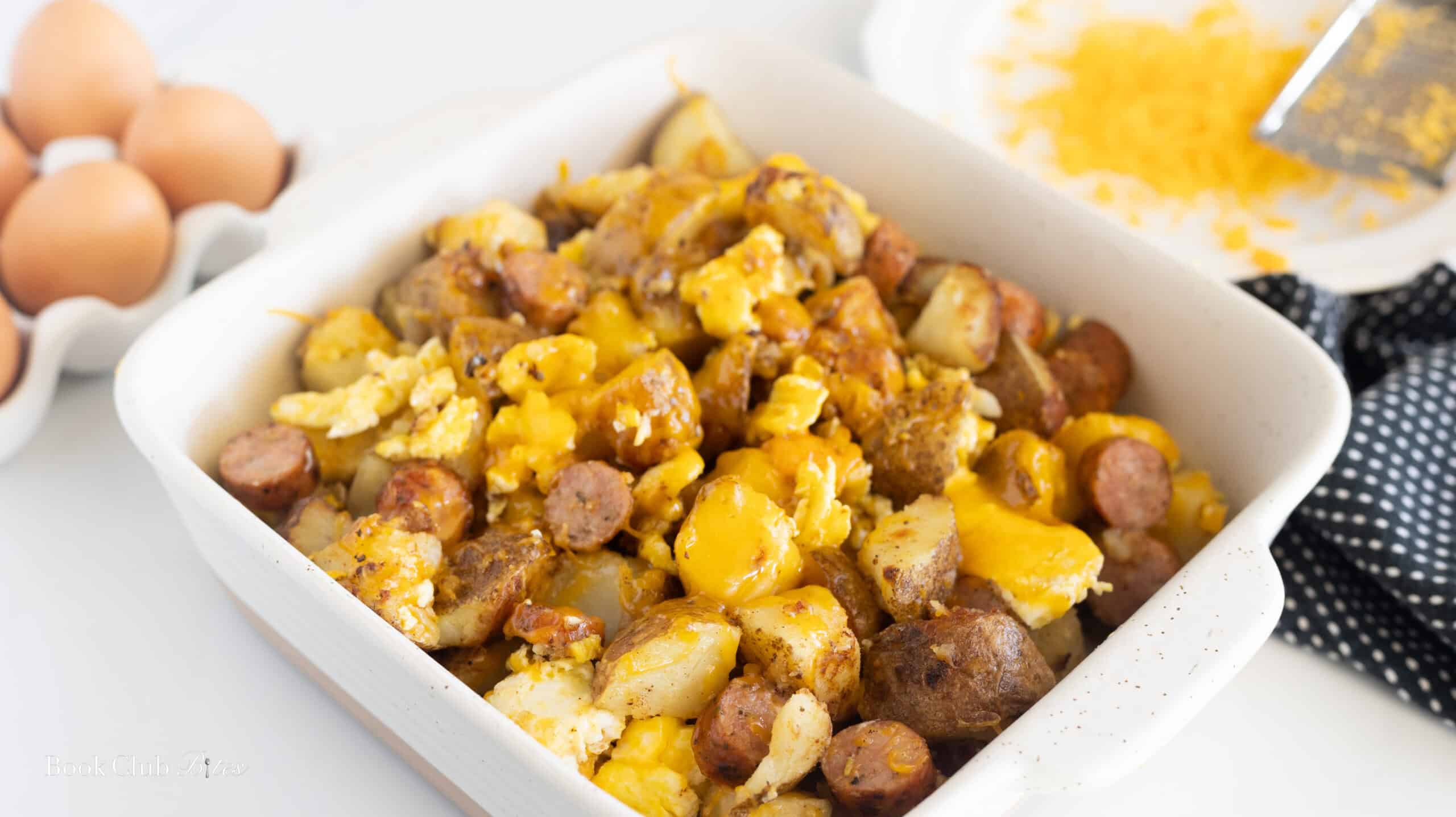 Creamy scrambled eggs with sausage and potatoes served in a white baking dish, garnished with melted cheese, perfect for breakfast or brunch.