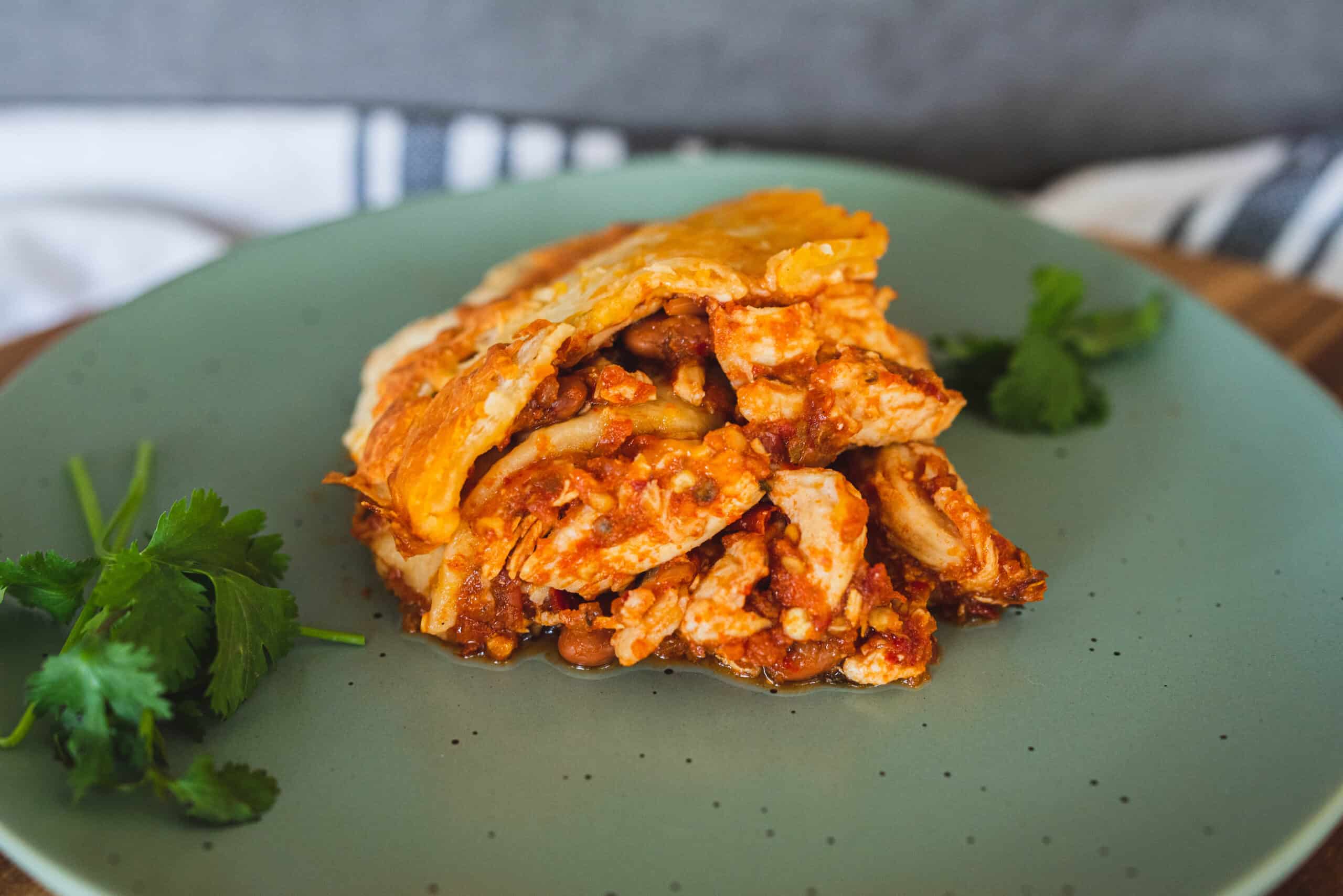 Savory layered chicken casserole with cheese and tomato sauce on green plate with cilantro garnish, hearty and flavorful comfort food, easy to prepare and perfect for family dinner or weekend meal, Hey Recipe.