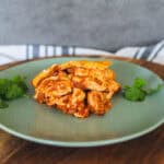 Savory chicken enchiladas with melted cheese on green ceramic plate, fresh cilantro garnish, served on wooden platter, Mexican-inspired comfort food, delicious homemade enchiladas, spice and flavorful ingredients, hearty and cheesy Mexican dish.