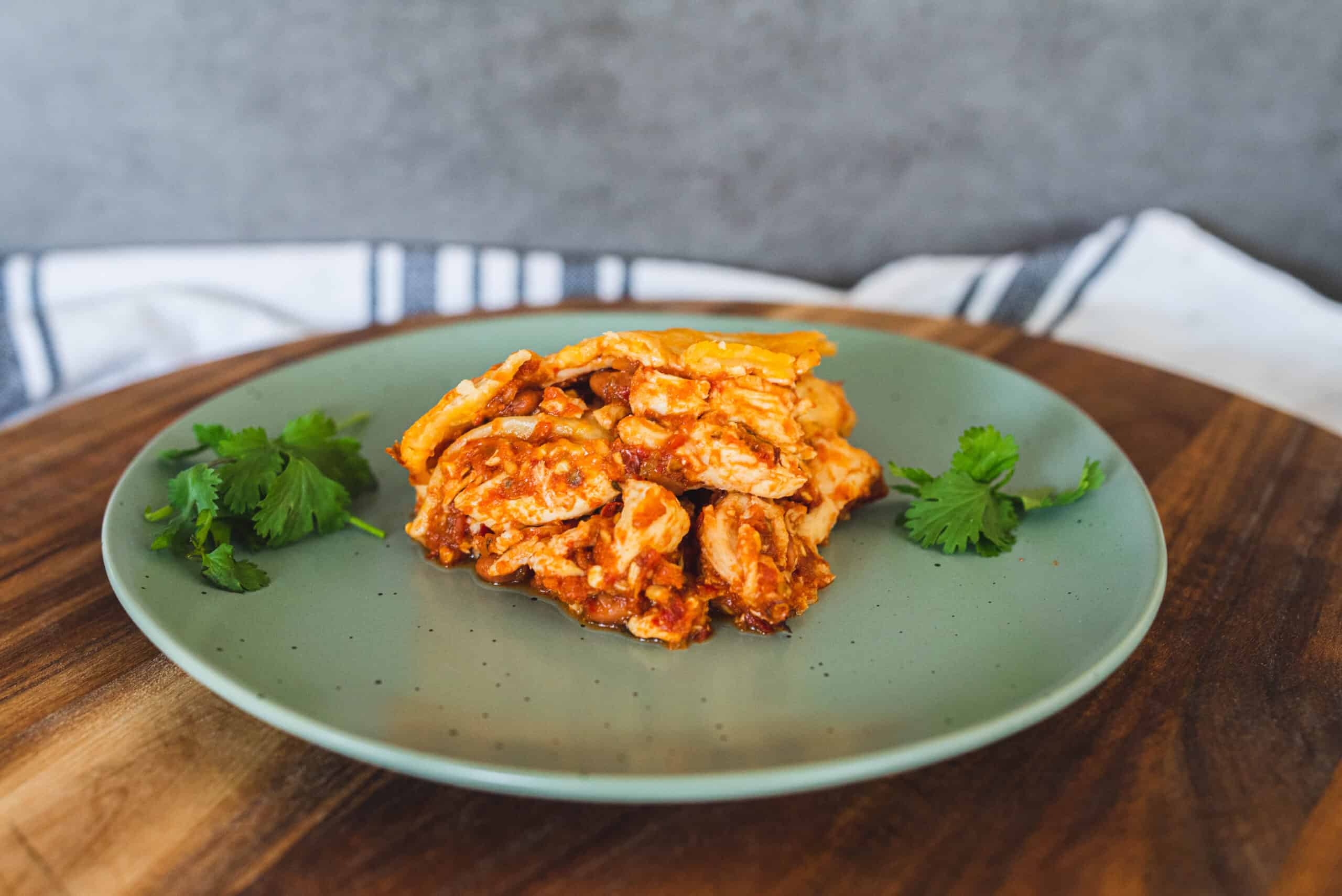 Savory chicken enchiladas with melted cheese on green ceramic plate, fresh cilantro garnish, served on wooden platter, Mexican-inspired comfort food, delicious homemade enchiladas, spice and flavorful ingredients, hearty and cheesy Mexican dish.