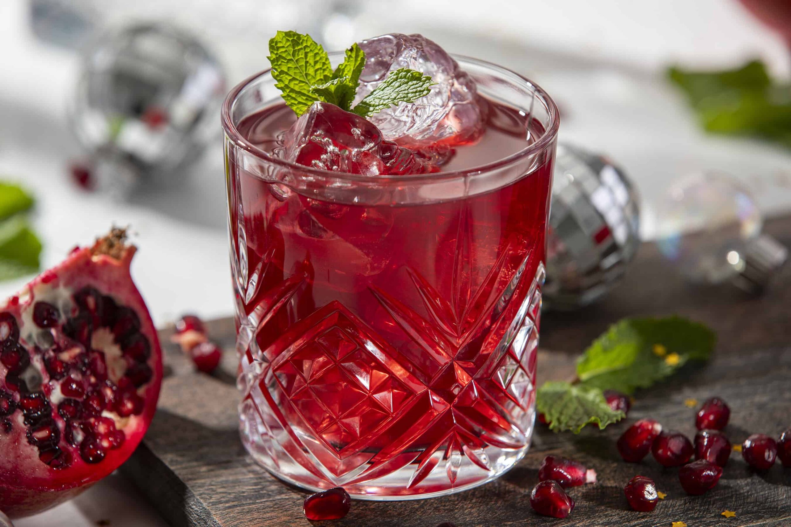 Fresh pomegranate cocktail with ice, mint garnish, and vibrant red color on a rustic wooden surface.