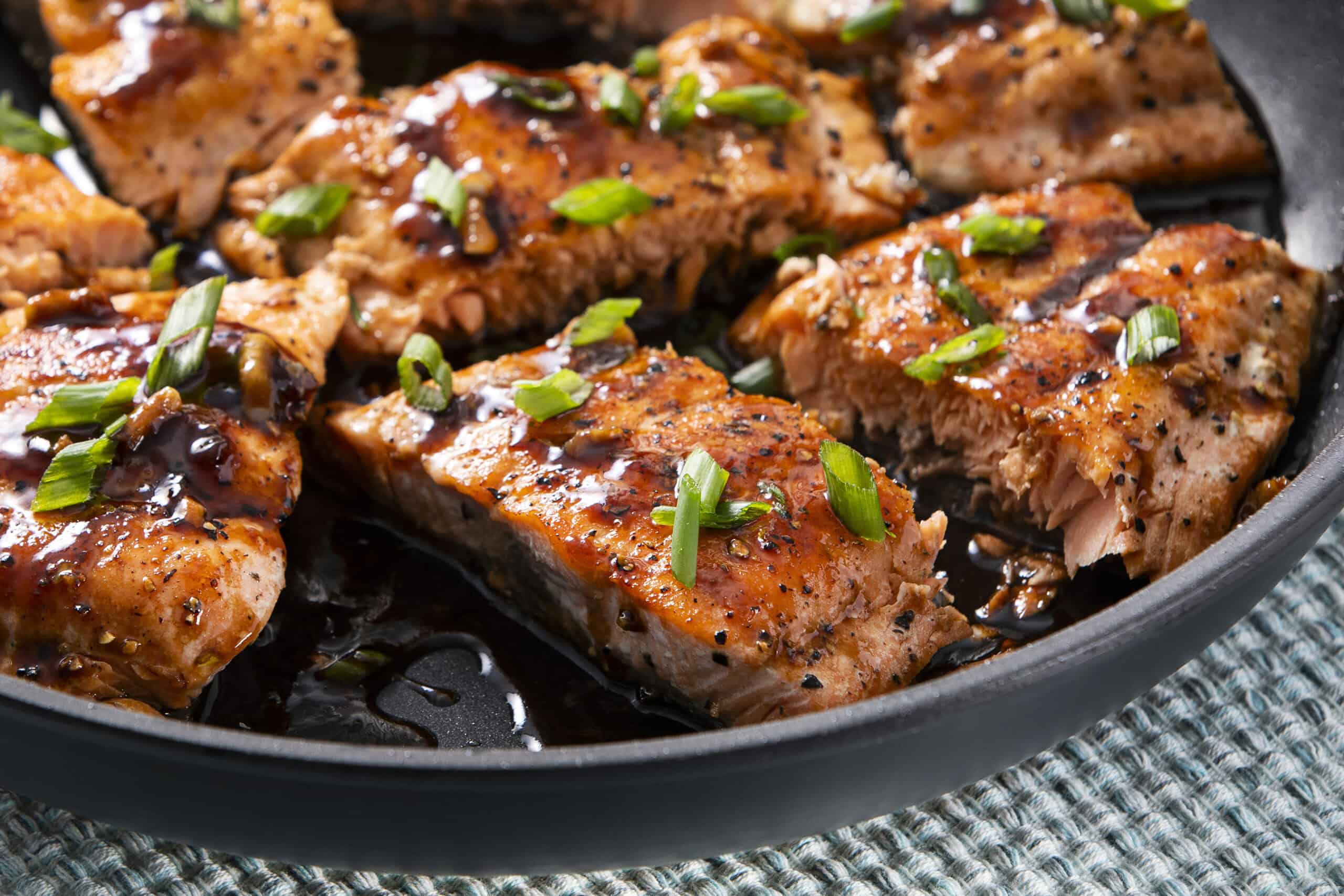 Juicy pan-seared salmon fillets with a glossy glaze, topped with fresh chopped green onions, served in a black skillet for a healthy and delicious seafood dinner.