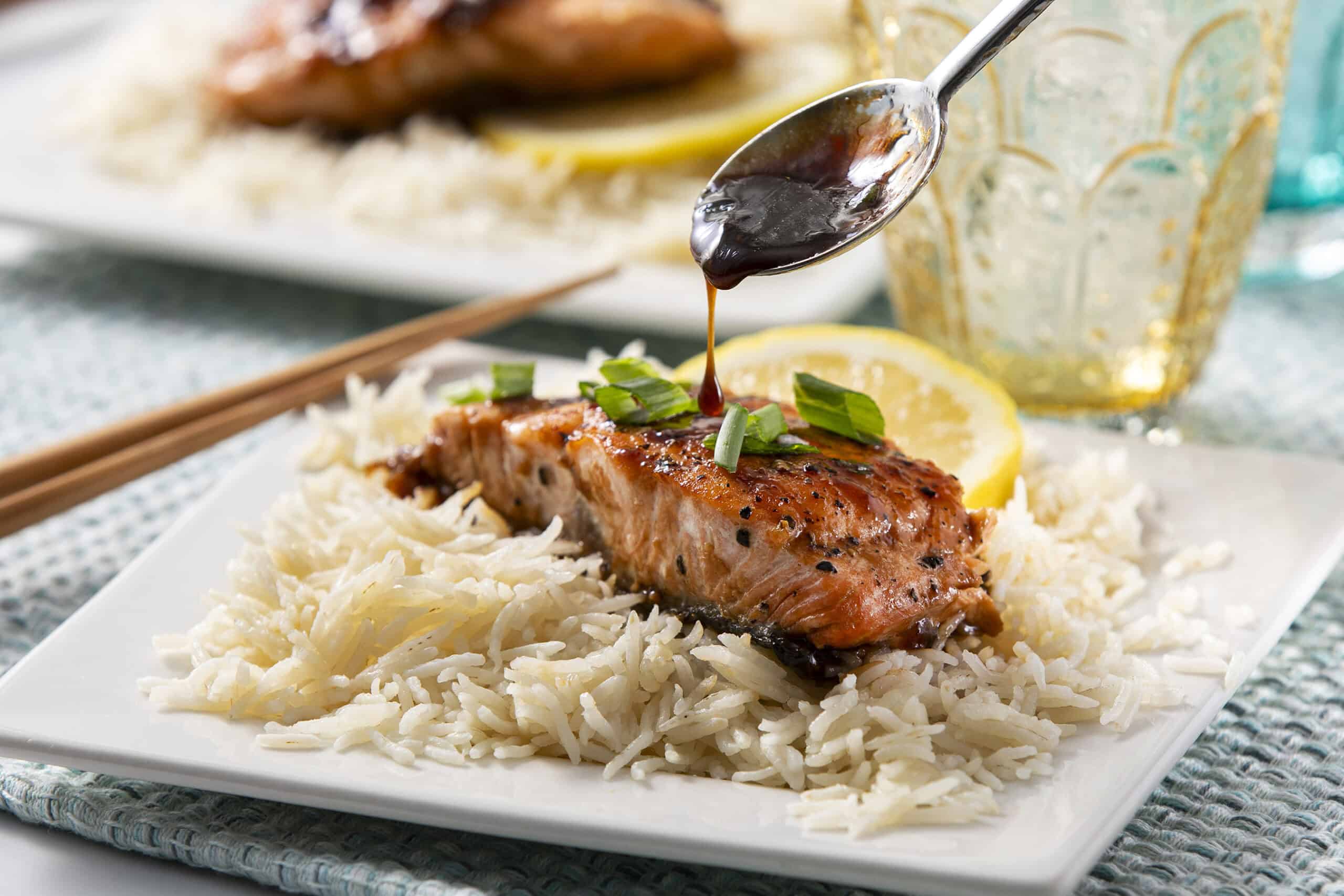 Succulent grilled salmon steak topped with savory sauce, served over fluffy white rice with lemon slices and fresh green onions on a white plate.