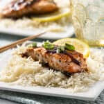 Succulent grilled salmon served over fluffy white rice with a drizzle of balsamic glaze, garnished with chopped scallions and lemon slices for a delightful seafood meal.