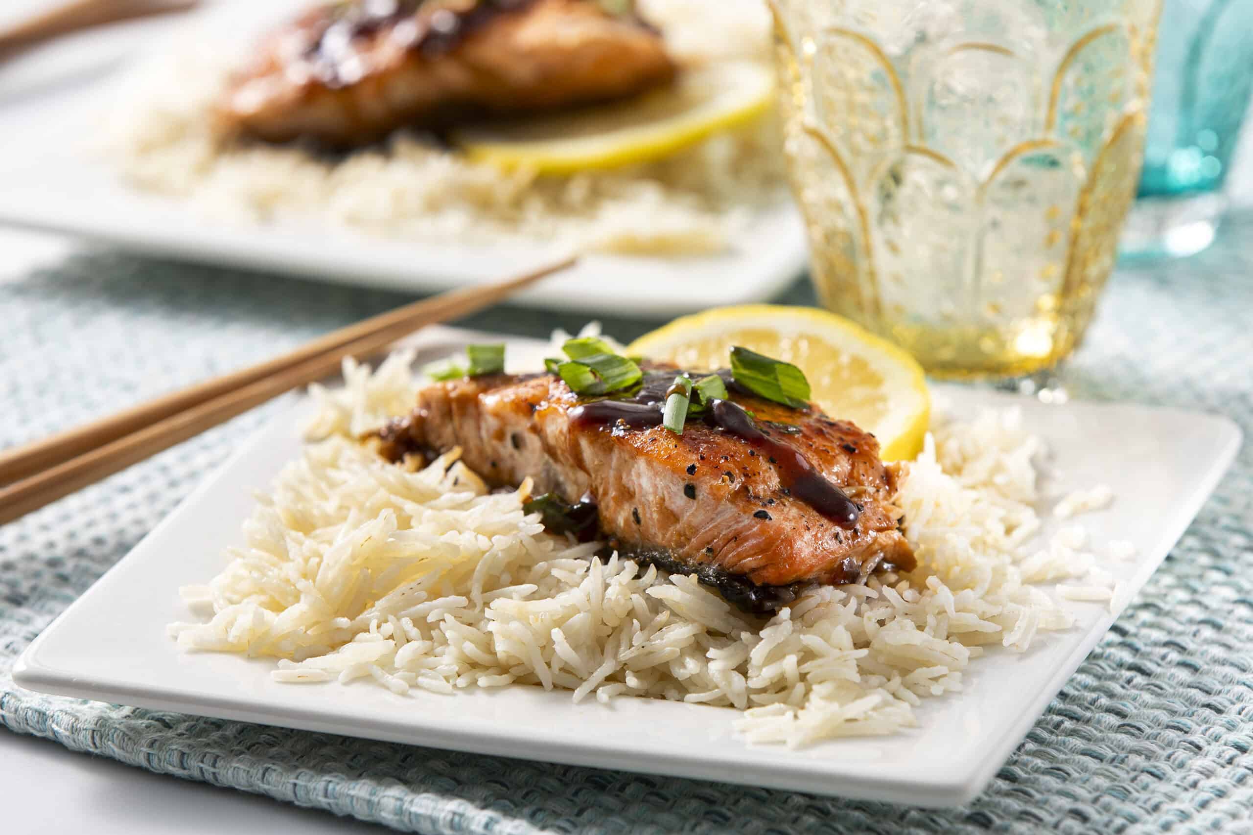 Succulent grilled salmon served over fluffy white rice with a drizzle of balsamic glaze, garnished with chopped scallions and lemon slices for a delightful seafood meal.