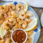 Juicy grilled shrimp with lemon wedges, served with a side of spicy cocktail sauce on a decorative plate. Perfect for seafood lovers and appetizer recipes.