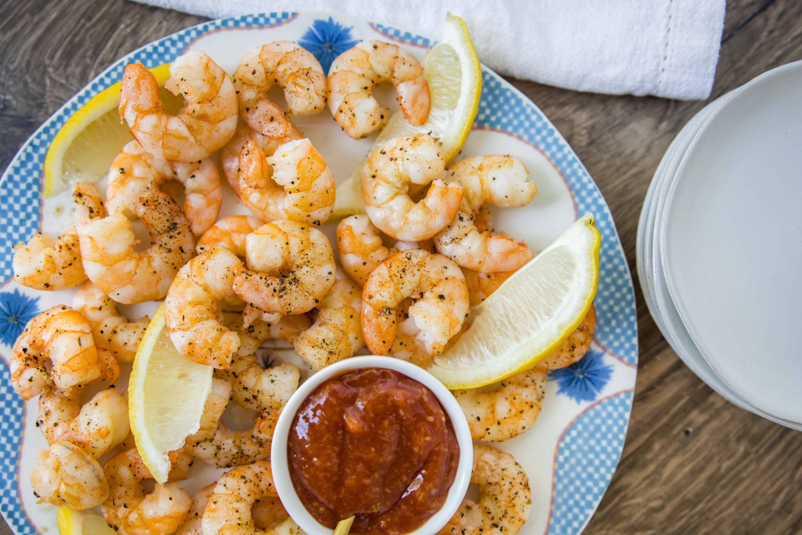 Juicy grilled shrimp with lemon wedges, served with a side of spicy cocktail sauce on a decorative plate. Perfect for seafood lovers and appetizer recipes.