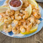 Juicy shrimp tempura with lemon wedges and a side of spicy dipping sauce on a colorful plate, served on a rustic wooden table. Perfect for seafood lovers and appetizer recipes.