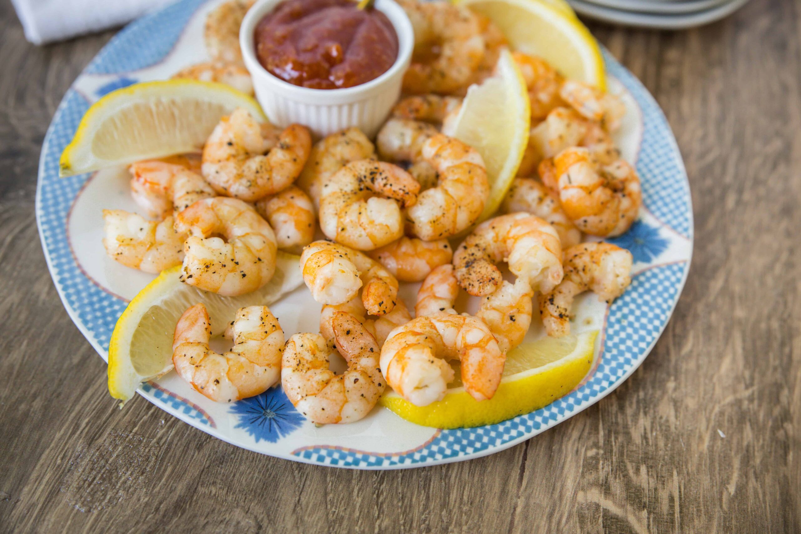 Juicy shrimp tempura with lemon wedges and a side of spicy dipping sauce on a colorful plate, served on a rustic wooden table. Perfect for seafood lovers and appetizer recipes.