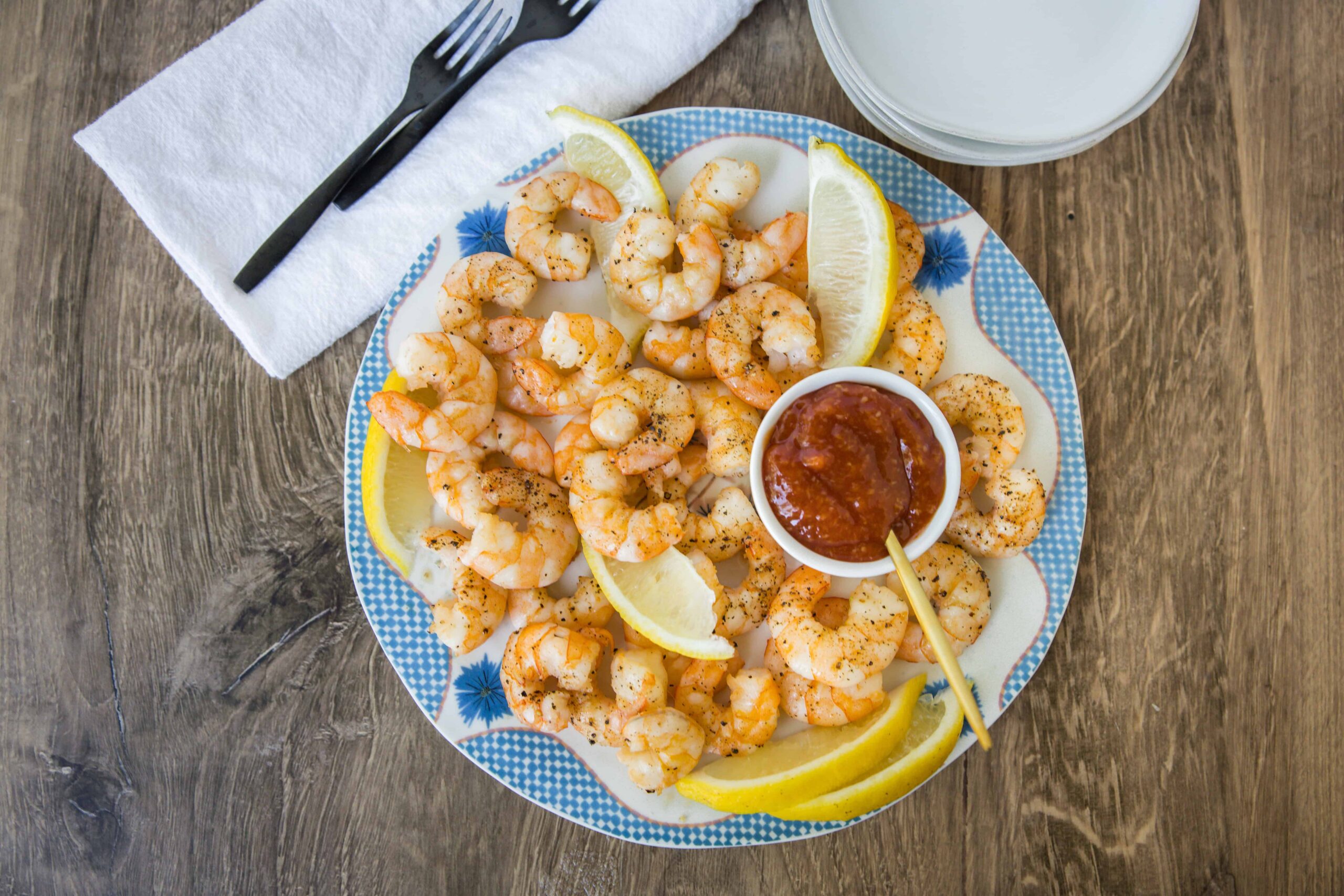 Succulent shrimp cooked with spices served with lemon wedges and spicy dipping sauce on a decorative plate. Perfect for seafood lovers and appetizer recipes.