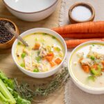 Savory chicken vegetable soup bowls with fresh carrots, celery, and herbs, seasoned with salt and pepper, featuring ingredients like olive oil and peas, served in white bowls on a wooden table.