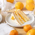 Fresh lemon layer cake with citrus filling and creamy frosting, served on a white plate with whole lemons around, perfect for spring desserts.