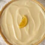 Lemon cheesecake with smooth lemon curd topping and a lemon wedge garnish on a lace doily.