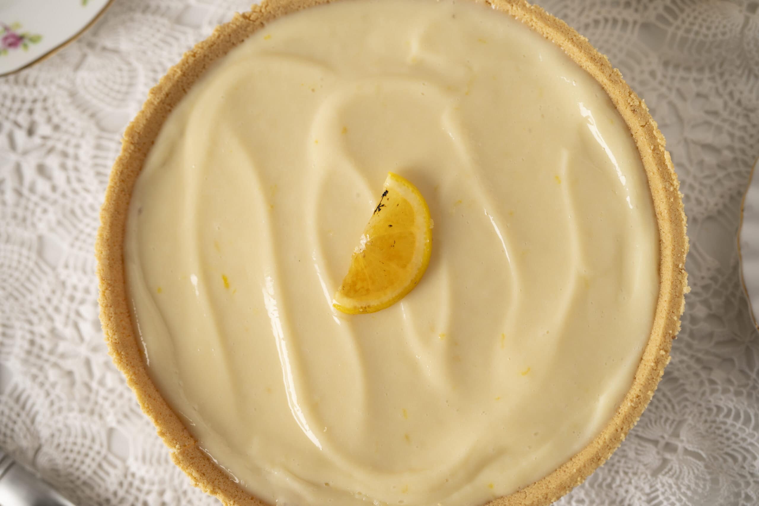 Lemon cheesecake with smooth lemon curd topping and a lemon wedge garnish on a lace doily.