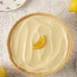 Lemon tart with a smooth, creamy lemon filling and a crumbly crust, garnished with a lemon wedge on top. Fresh lemons and vintage floral china add a charming touch to this classic dessert.