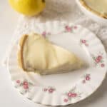Creamy lemon cheesecake slice on floral china plate, perfect for summer dessert. Fresh lemon and rich cheesecake flavor with smooth texture, served with a vintage touch.