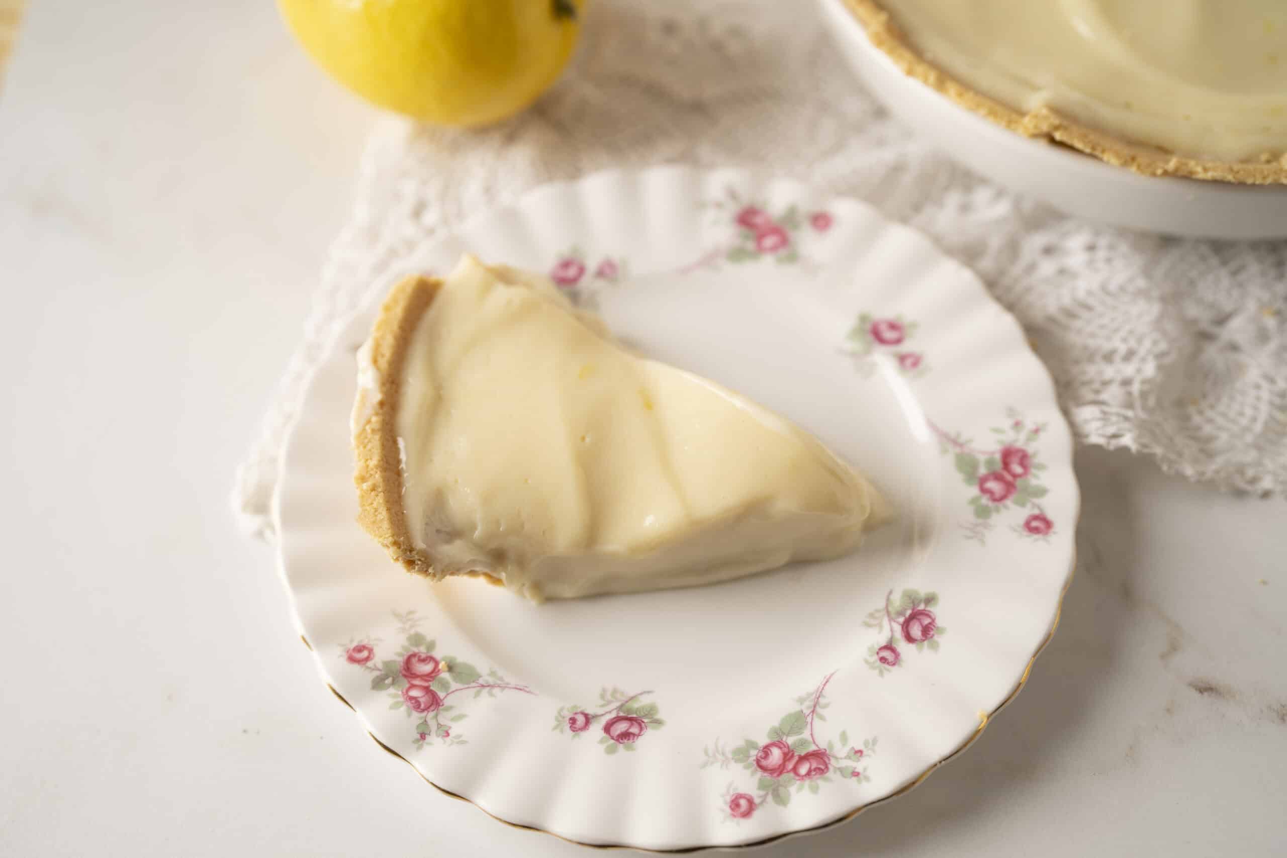 Creamy lemon cheesecake slice on floral china plate, perfect for summer dessert. Fresh lemon and rich cheesecake flavor with smooth texture, served with a vintage touch.