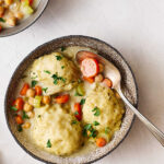 Creamy chicken and mashed potato casserole with vegetables, chickpeas, carrots, and herbs in a rustic bowl on a white textured surface. Perfect comfort food recipe with a rich, flavorful sauce.