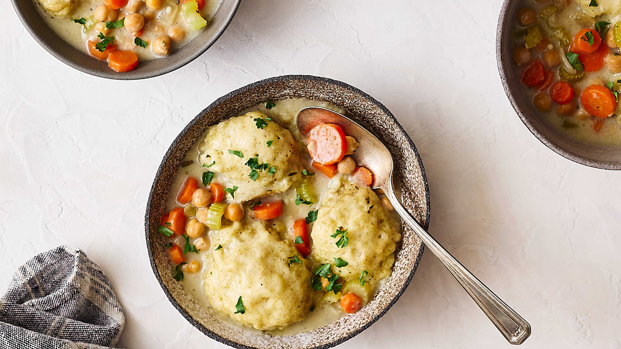 Creamy chicken and mashed potato casserole with vegetables, chickpeas, carrots, and herbs in a rustic bowl on a white textured surface. Perfect comfort food recipe with a rich, flavorful sauce.