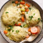 Creamy chicken and vegetable pot pie with tender chicken, carrots, and celery in a savory sauce, served in a rustic black skillet garnished with fresh herbs for a comforting homemade meal.
