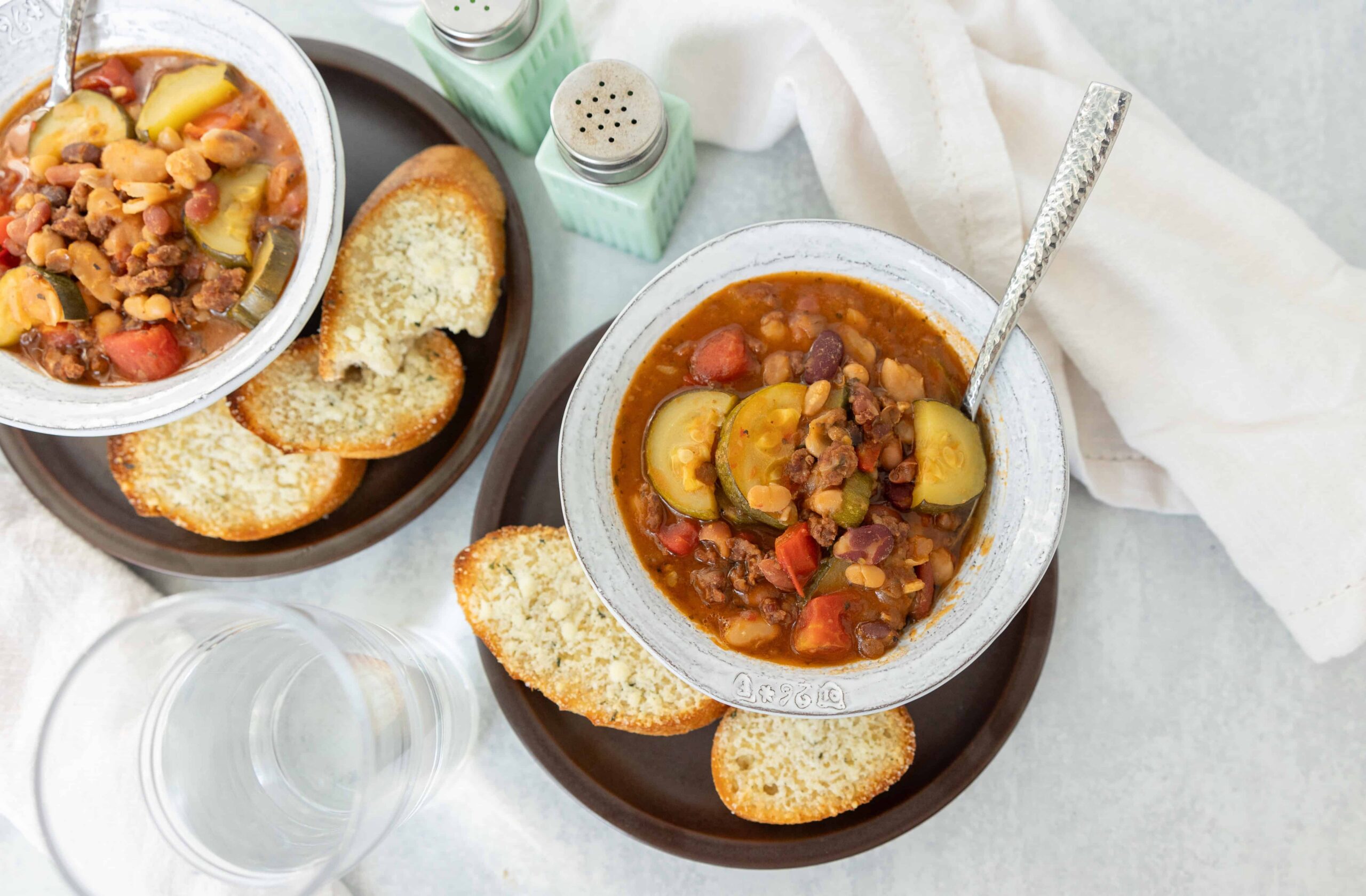 Hearty vegetable bean soup served with toasted garlic bread slices on a dark plate, fresh and flavorful, perfect for a comforting meal.
