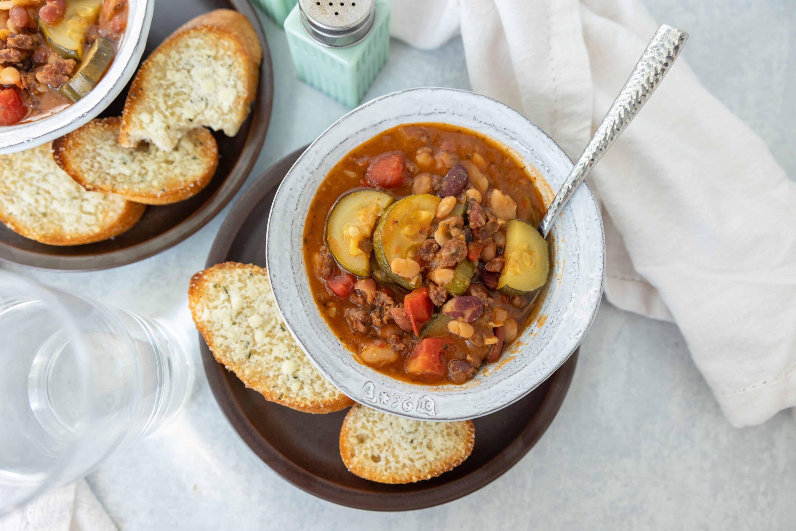 Creamy vegetable beef stew with zucchini, tomatoes, and beans served with toasted garlic bread on a rustic plate. Perfect comfort food recipe for cold days or family dinners.
