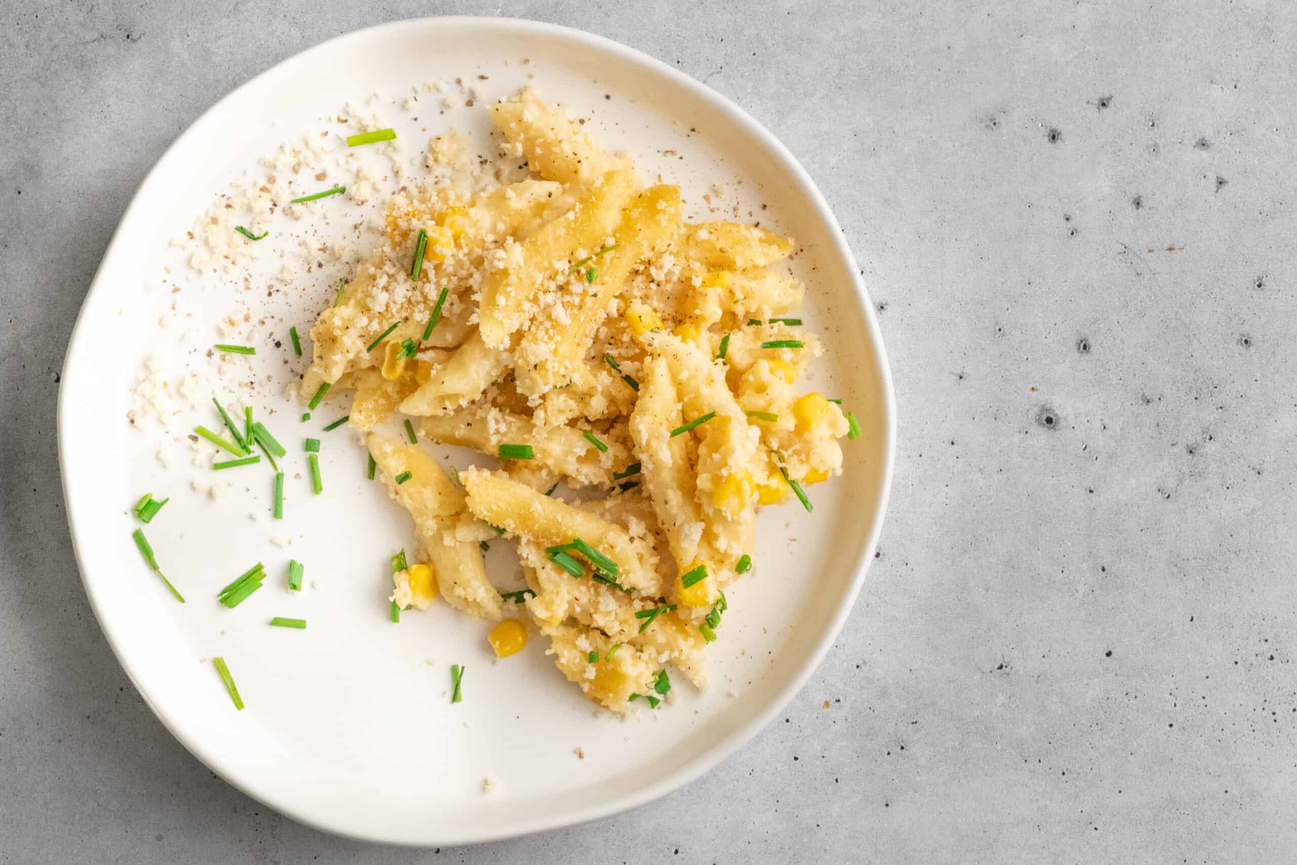Delicious creamy pasta with grated cheese, chopped chives, and corn served on a white plate. Perfect for quick homemade Italian comfort food or family dinner recipes.