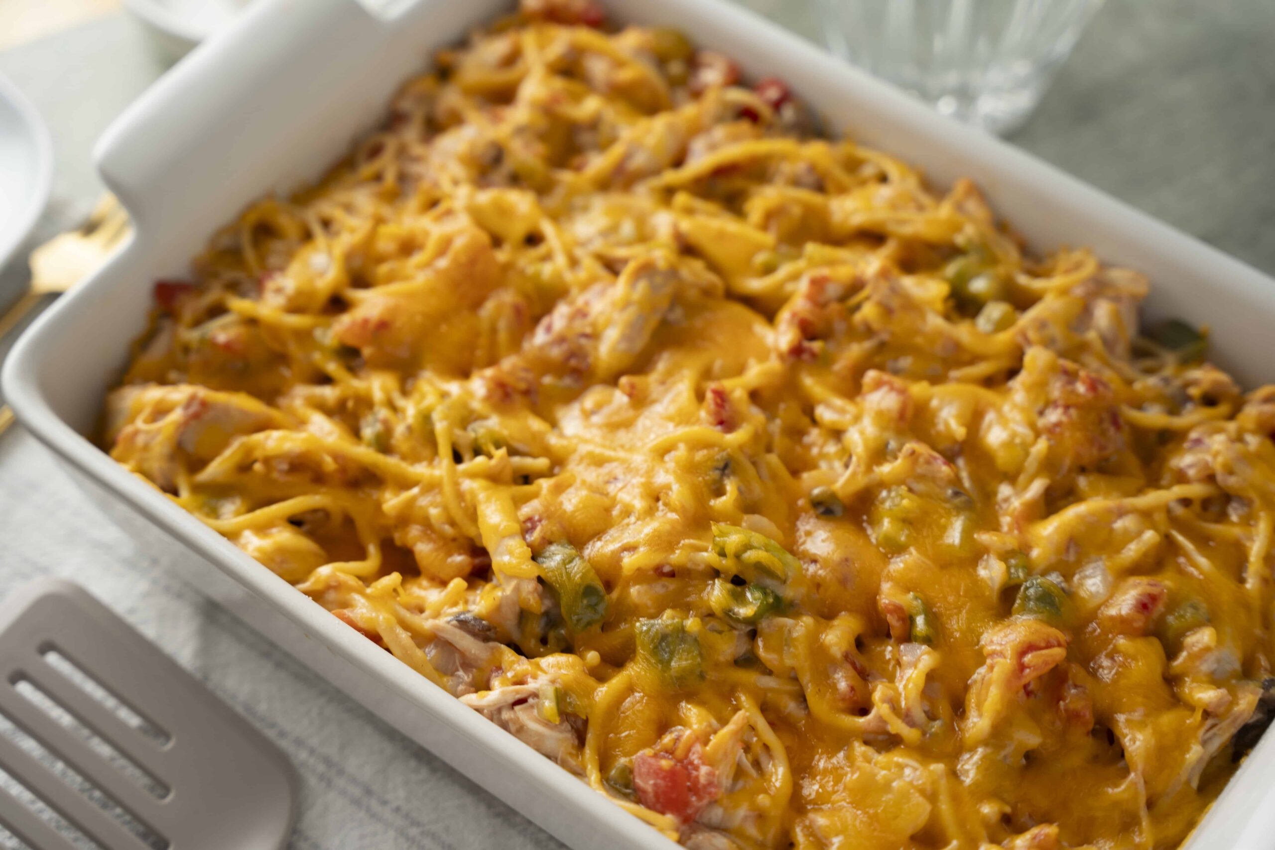 Creamy baked chicken spaghetti casserole with melted cheese and vegetables, served in a white baking dish, ideal for family dinners and comfort food recipes.