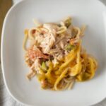 Tender shredded chicken and creamy cheese on a bed of spaghetti with fresh vegetables, served on a white plate for a delicious homemade meal.