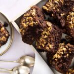 Rich and fudgy double chocolate brownie bars topped with chopped nuts, served on a black tray and a small plate, perfect for chocolate lovers and dessert recipes.
