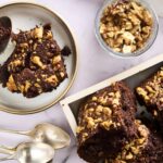 Rich chocolate walnut brownie with chopped walnuts on top, served on a white plate with a spoon, accompanied by more brownies and a jar of chopped walnuts, perfect for dessert or snack.