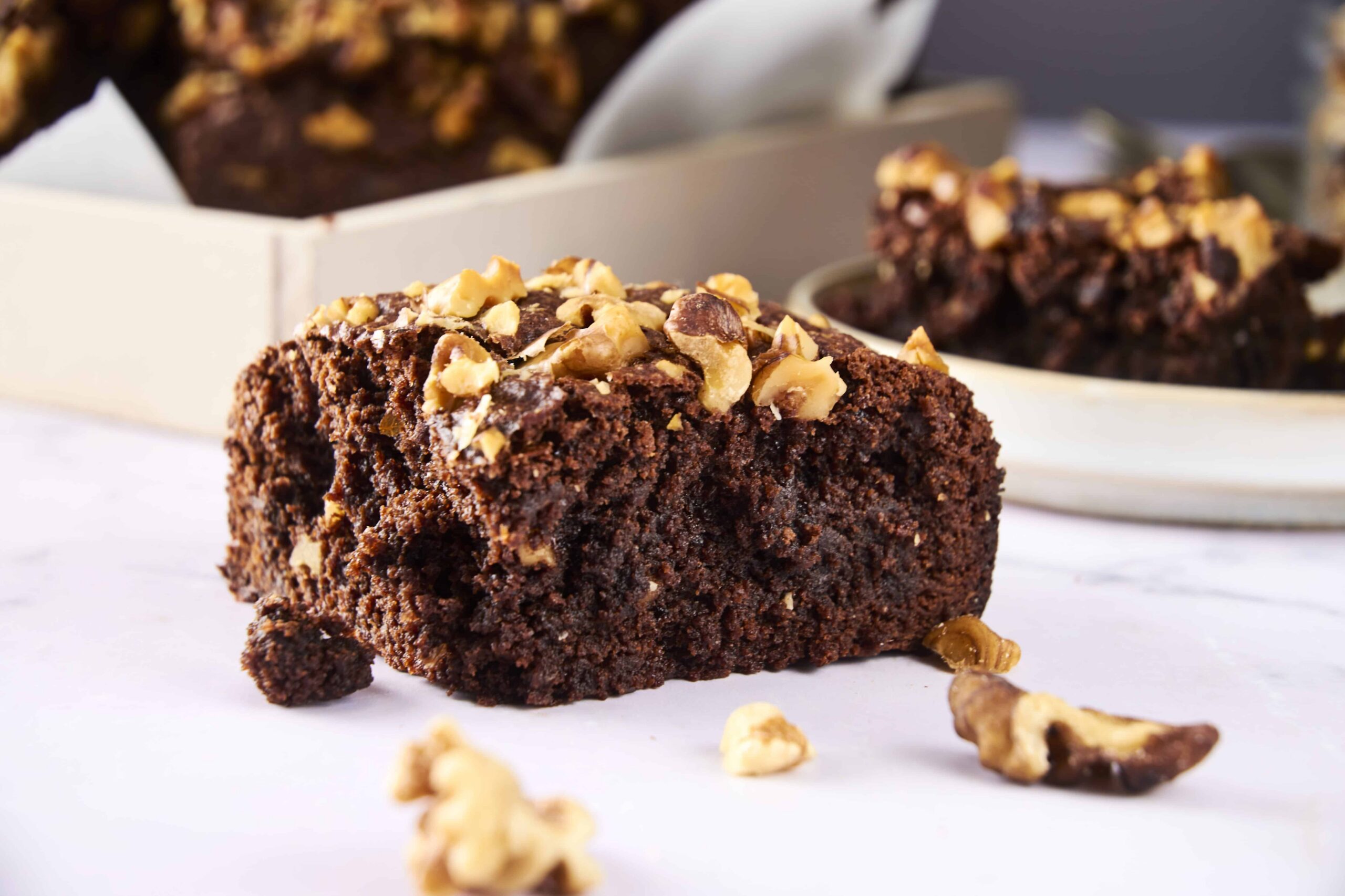 Rich, gooey chocolate brownie topped with chopped walnuts, close-up of a freshly baked chocolate walnut brownie slice, decadent homemade chocolate brownie with walnuts on white baking paper, relevance.