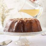 Butterscotch sauce is poured over a moist, rich cake on a glass cake stand, creating a decadent dessert perfect for celebrations and sweet cravings, with a soft, tender texture and luscious caramel flavor.