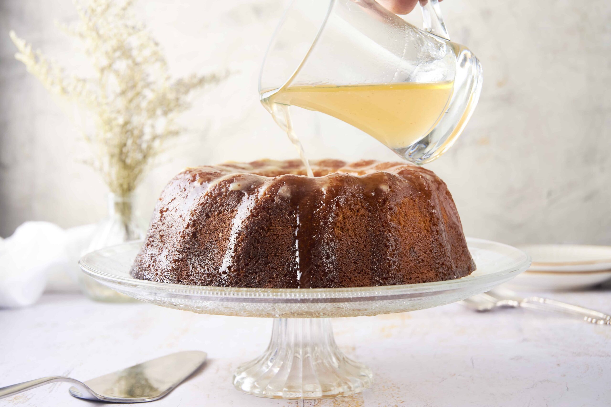 Butterscotch sauce is poured over a moist, rich cake on a glass cake stand, creating a decadent dessert perfect for celebrations and sweet cravings, with a soft, tender texture and luscious caramel flavor.