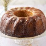 Golden brown Bundt cake with a glaze on a glass cake stand, showcasing a moist, delicious dessert perfect for baking enthusiasts and dessert lovers.