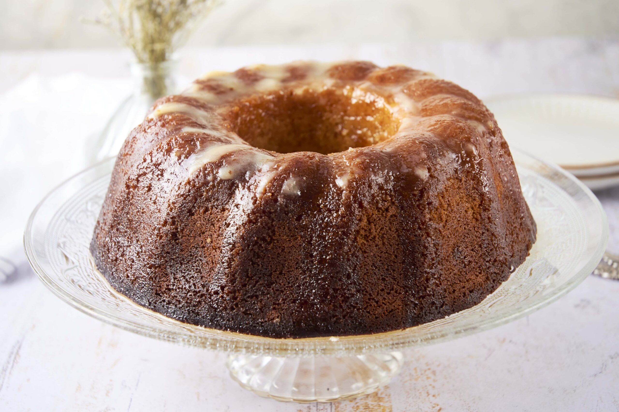 Golden brown Bundt cake with a glaze on a glass cake stand, showcasing a moist, delicious dessert perfect for baking enthusiasts and dessert lovers.