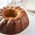Rich caramel bundt cake with a glaze, served on a glass cake stand, perfect for dessert or special occasions. The cake has a moist, golden-brown interior and is drizzled with sweet icing.