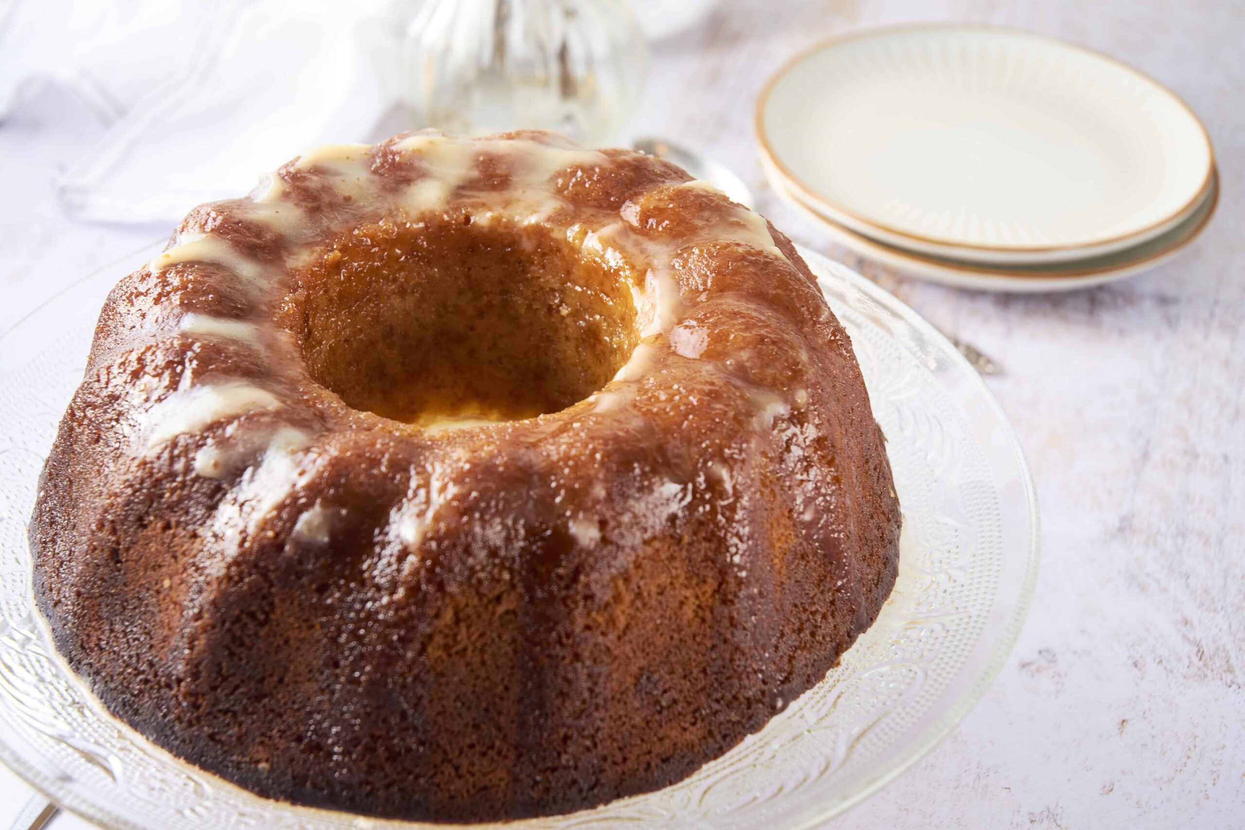 Rich caramel bundt cake with a glaze, served on a glass cake stand, perfect for dessert or special occasions. The cake has a moist, golden-brown interior and is drizzled with sweet icing.