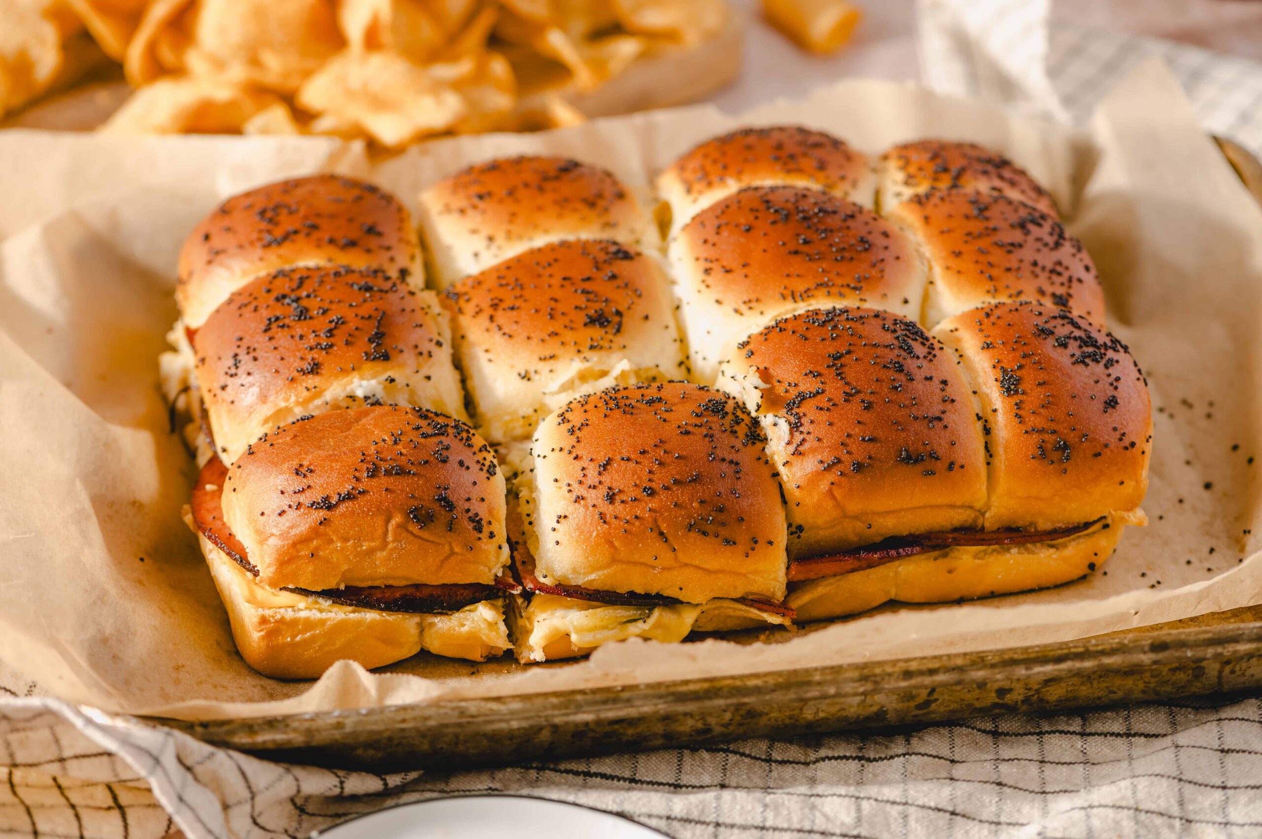 Golden brown dinner rolls topped with poppy seeds, baked to perfection in a parchment-lined tray. Soft, fluffy bread with a slightly crisp crust, ideal for breakfast or dinner.