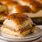 Savory potato bread roll sandwich with ham and melted cheese on a white saucer. Indulge in a delicious, hearty breakfast or snack featuring soft bread, ham, and creamy cheese, perfect for comfort food lovers.