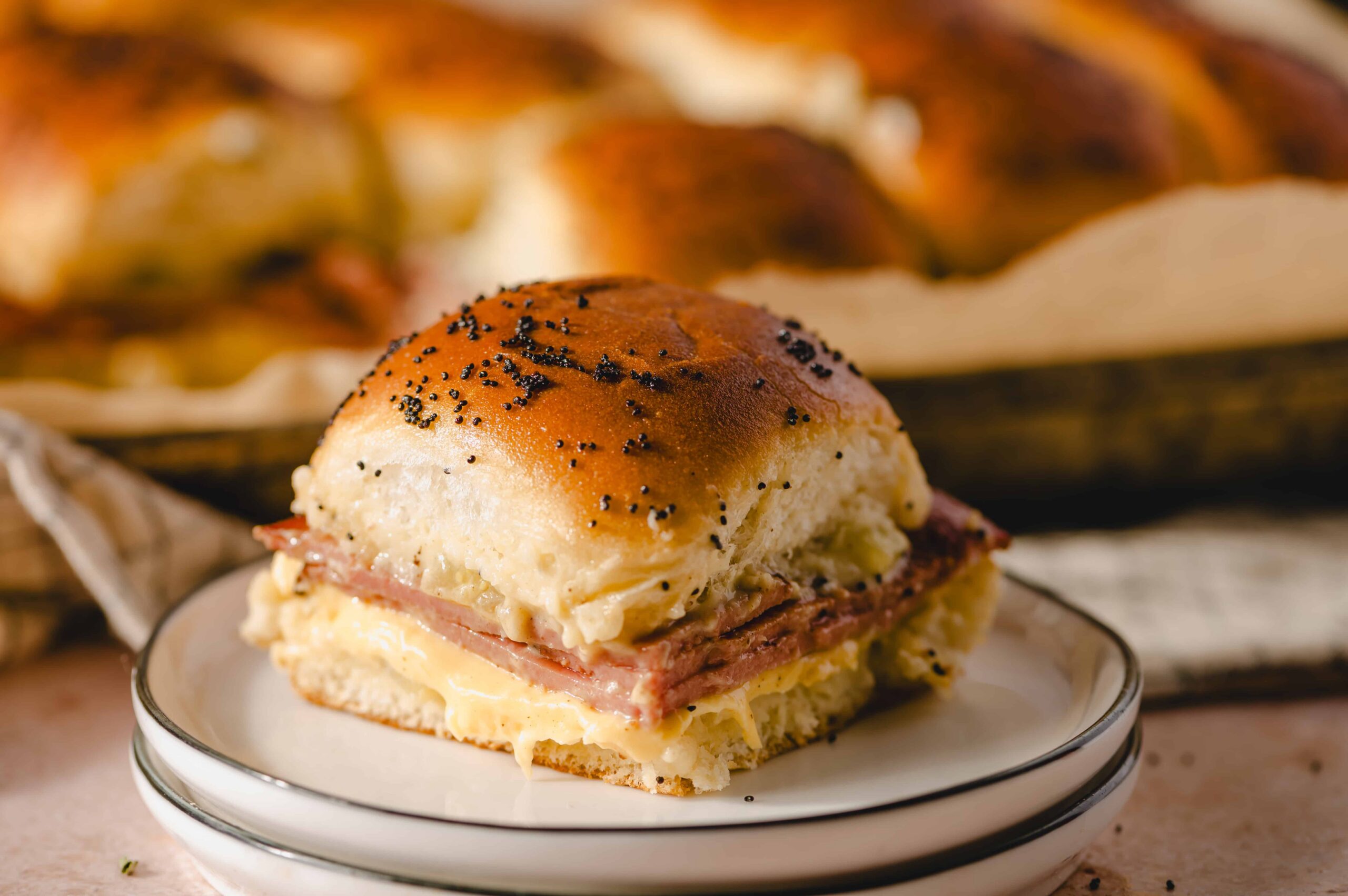 Savory potato bread roll sandwich with ham and melted cheese on a white saucer. Indulge in a delicious, hearty breakfast or snack featuring soft bread, ham, and creamy cheese, perfect for comfort food lovers.