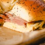 Savory breakfast sandwich with egg, ham, and melted cheese on toasted poppy seed bun, close-up.