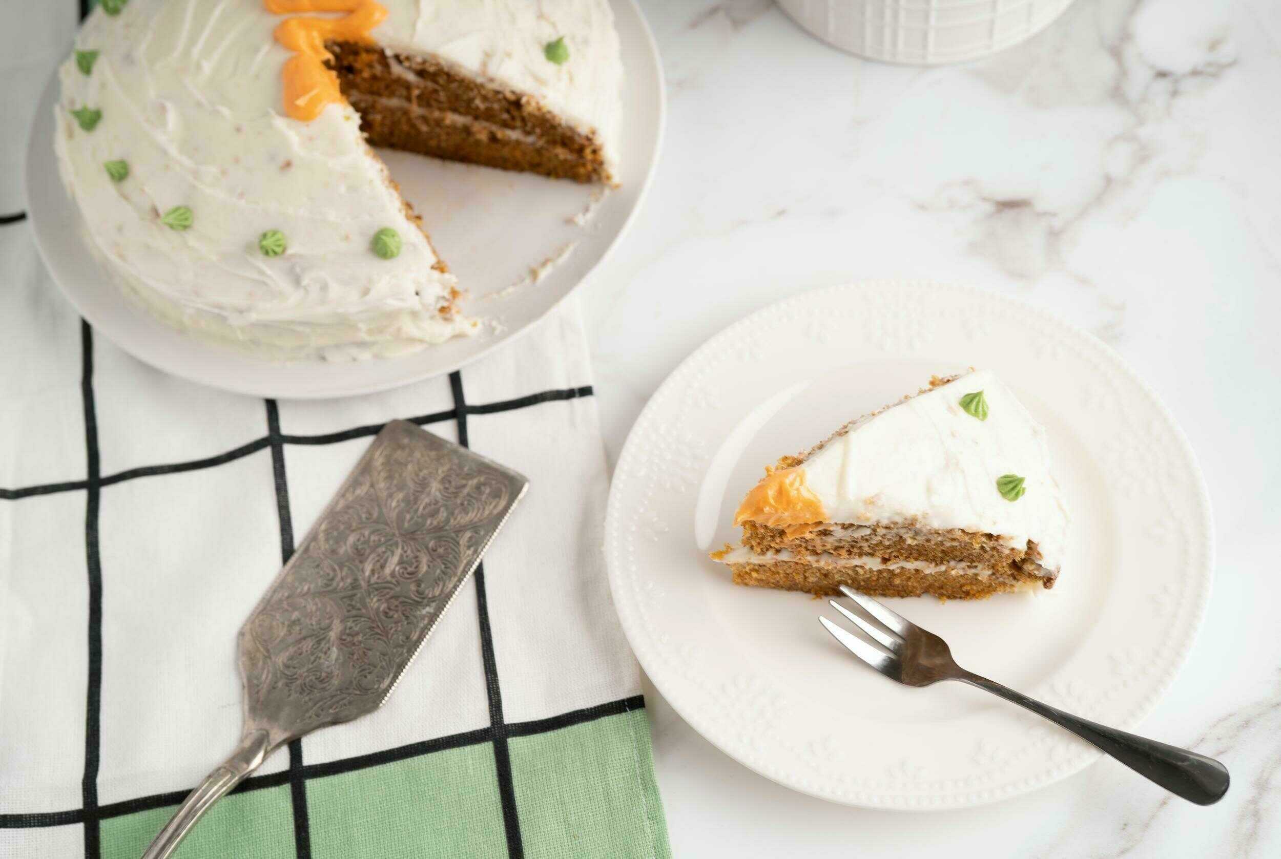 Delicious carrot cake with cream cheese frosting on a white plate, showcasing a moist texture and topped with small green leaves, served on a marble countertop.